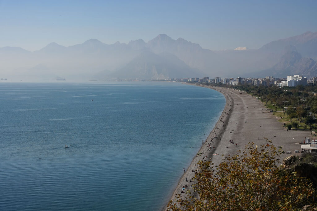 A panoramic view of Konyaaltı Beach in Antalya with turquoise waters and the Taurus Mountains in the background.